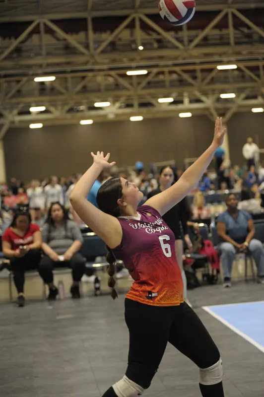 A Wolfpack Coquí player serves at a large tournament hall
