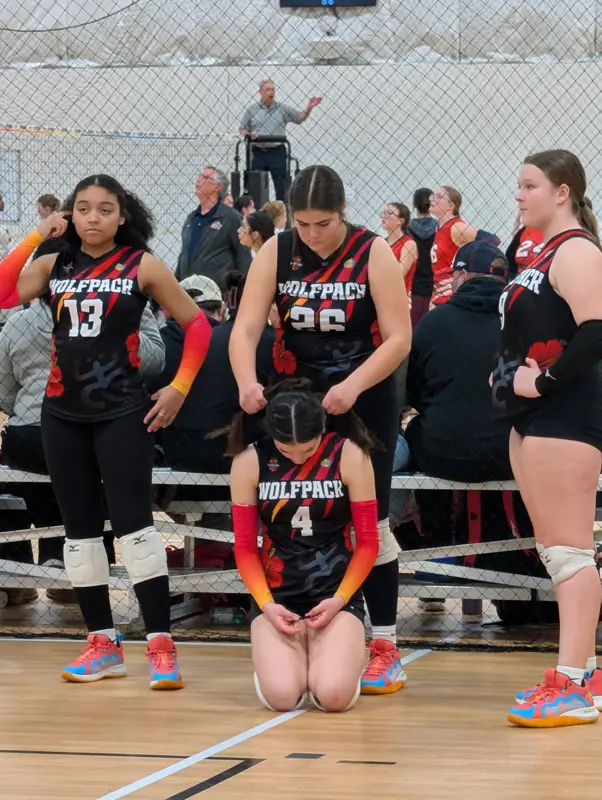 Teammates help braid a player's hair on the sideline