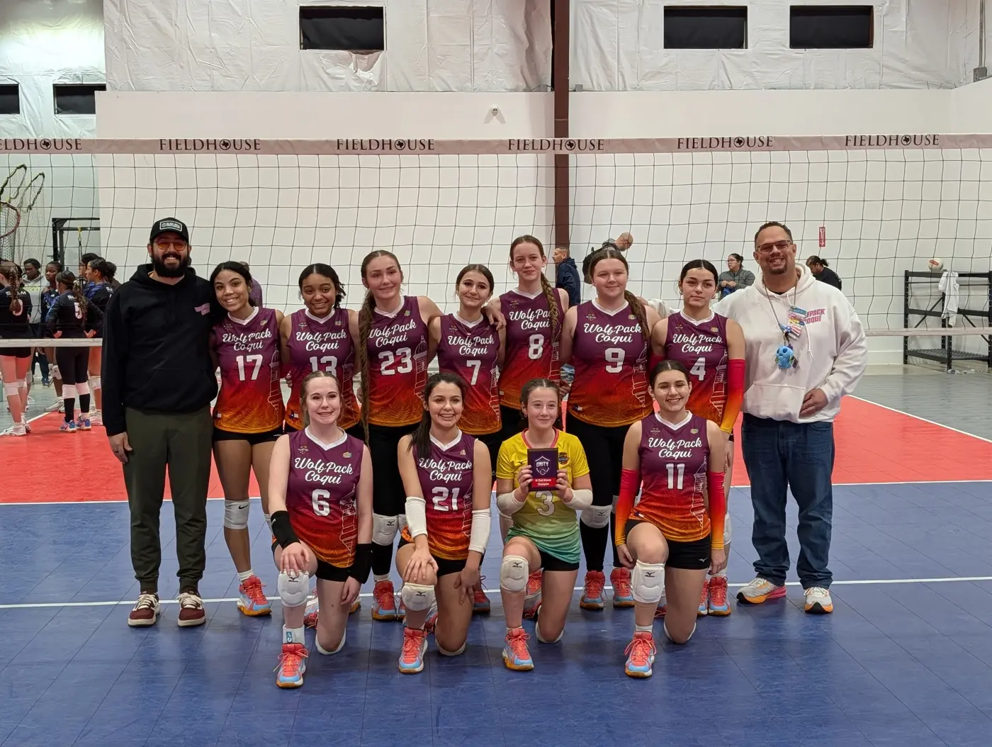 A Wolfpack Coquí team in orange-to-purple jerseys with its two coaches on a tournament court