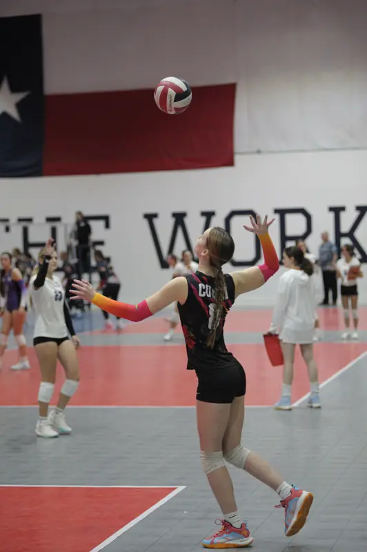 A Wolfpack Coquí player serves in a gym hung with a Texas flag